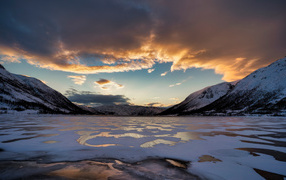 Ice-covered lake near the mountains at sunset