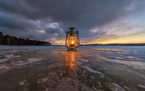 A kerosene lamp stands on the ice-covered shore