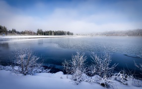 Покрытая льдом река  с заснеженными берегами зимой