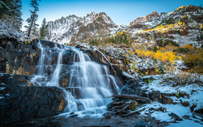 Красивый водопад стекает по холодным камням на фоне заснеженных гор