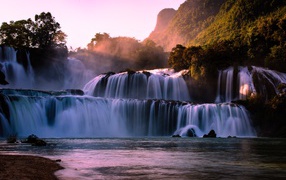 Каскадный водопад стекает по камням в лучах солнца 