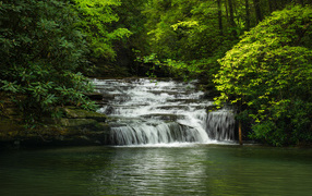 Водопад стекает по каменному каскаду в реку 