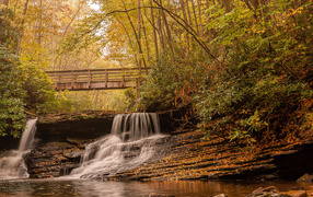 Водопад стекает по камням под мостом осенью