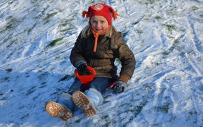 A little girl is rolling down a slide in the snow