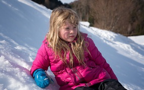 Маленькая девочка лежит на заснеженной горке 