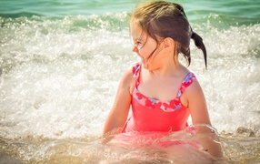 Веселая маленькая девочка в купальнике сидит в воде 