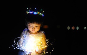 Маленькая девочка азиатка с гирляндой в руках на черном фоне