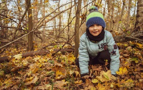 Маленький мальчик в лесу сидит на листве 