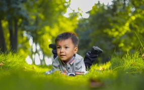 Маленький мальчик лежит на зеленой траве 