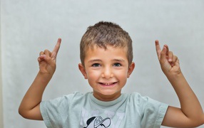 Маленький мальчик поднял руки вверх на сером фоне