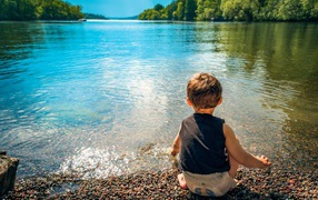 Маленький мальчик кидает камни в воду