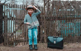 Маленький мальчик с чемоданом у забора