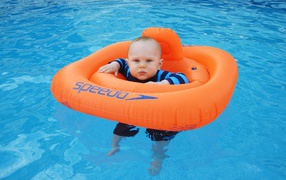 Маленький ребенок с оранжевым спасательным кругом в бассейне