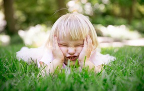 Маленькая смешная девочка лежит на зеленой траве 