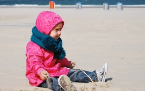 Маленькая девочка в розовой куртке на песке