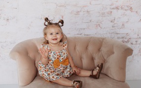 Маленькая девочка сидит на диване у стены