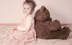 Маленькая девочка сидит с большим медведем