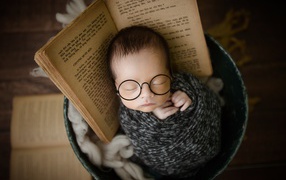 Маленький спящий ребенок в ведре с книгой 