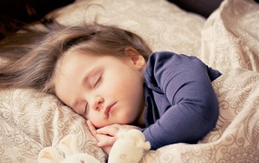 Маленькая спящая девочка на кровати с игрушкой 