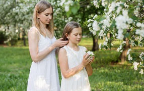 Мама заплетает дочке волосы у дерева