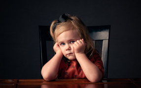 Грустная маленькая девочка сидит на черном стуле