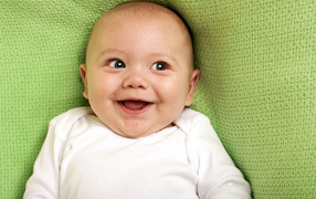 Улыбающийся маленький ребенок на зеленом покрывале 