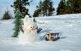 A toy snowman with a sled stands in the snow