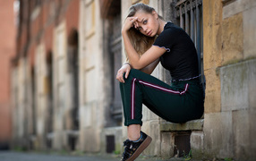 A girl in a tracksuit sits in front of a building