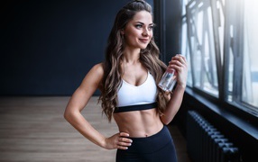 Красивая спортивная девушка с  бутылкой воды у окна