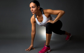 Девушка спортсменка в стойке на сером фоне 