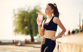 Спортивная девушка в черном пьет воду
