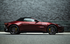 Красный автомобиль Aston Martin Vantage Roadster 2023 года на фоне стены