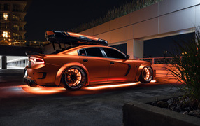 An orange Dodge Charger stands by the garage