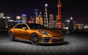 Золотистый автомобиль Porsche Panamera Turbo E-Hybrid 2024 года на фоне города