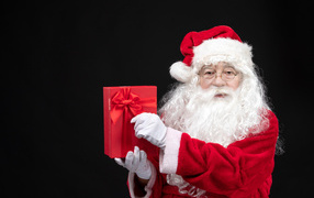 Санта Клаус с подарком в руках на черном фоне