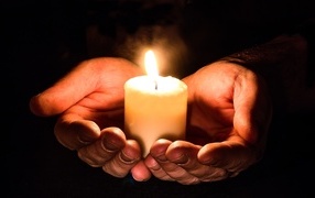A lit candle in the palms on a black background