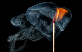 Lighted match with smoke on black background