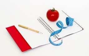 Notebook with a pen on the table with a centimeter and a tomato