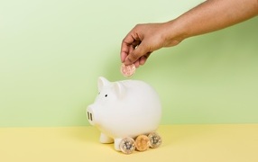 Hand throwing a coin into a piggy bank