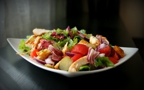 Аппетитный салат в белой тарелке на черном фоне