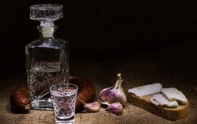 Бутылка водки на столе с салом, колбасой и чесноком