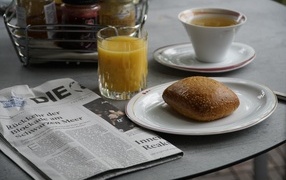 Булочка и стакан сока на столе с газетой