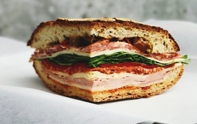 Кусок булки с колбасой, ветчиной и листьями салата