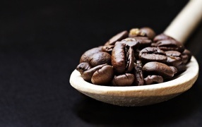 Зерна кофе на деревянной ложке на черном фоне