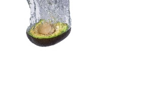 Half of an avocado falls into the water on a white background