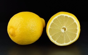 Large yellow lemon and half on a black background