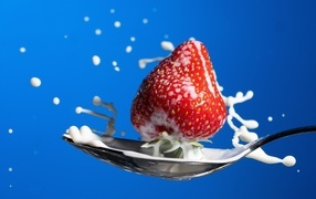 Молоко в ложке с клубникой на синем фоне