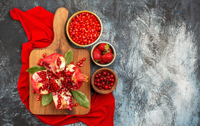 Peeled pomegranate on the table with strawberries and currants