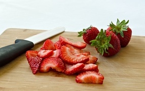 Red strawberries are sliced on a wooden board