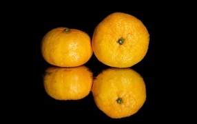 Two tangerines on a black mirror surface